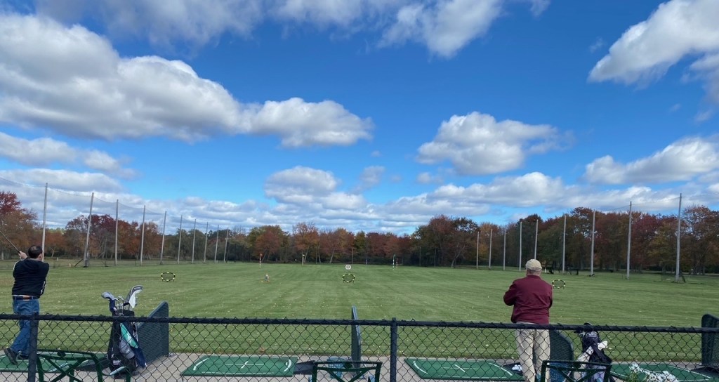 View of the driving range at Norwood Country Club from behind the fence. Golfers enjoy a day at the range.